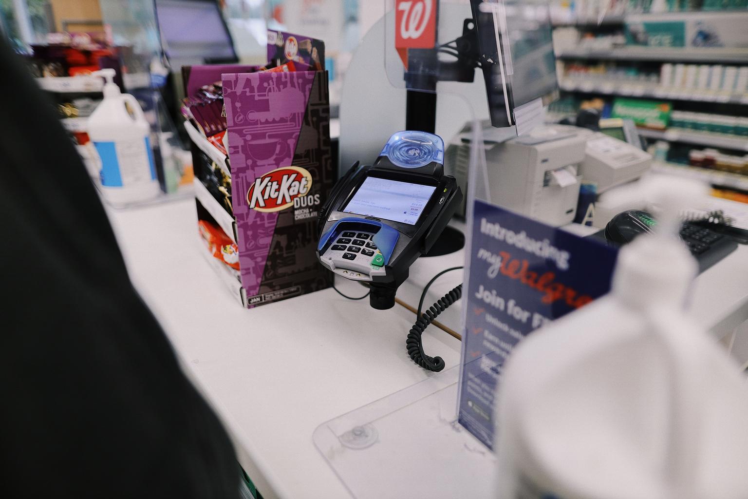 A payment-card terminal sits on a Walgreens checkout counter beside candy and retail displays.