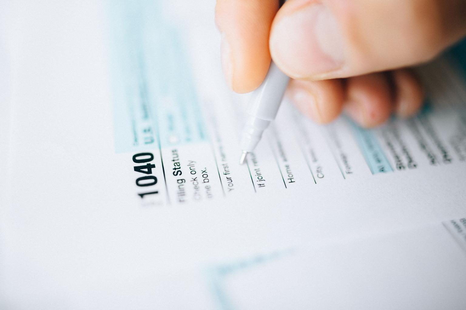 A hand holds a pen over the filing-status section of a U.S. Form 1040 tax return.