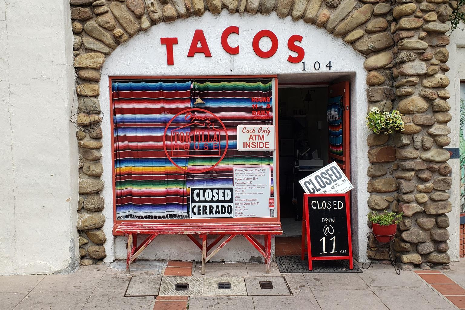 A closed taco storefront in Ojai, California, displays English and Spanish closed signs.