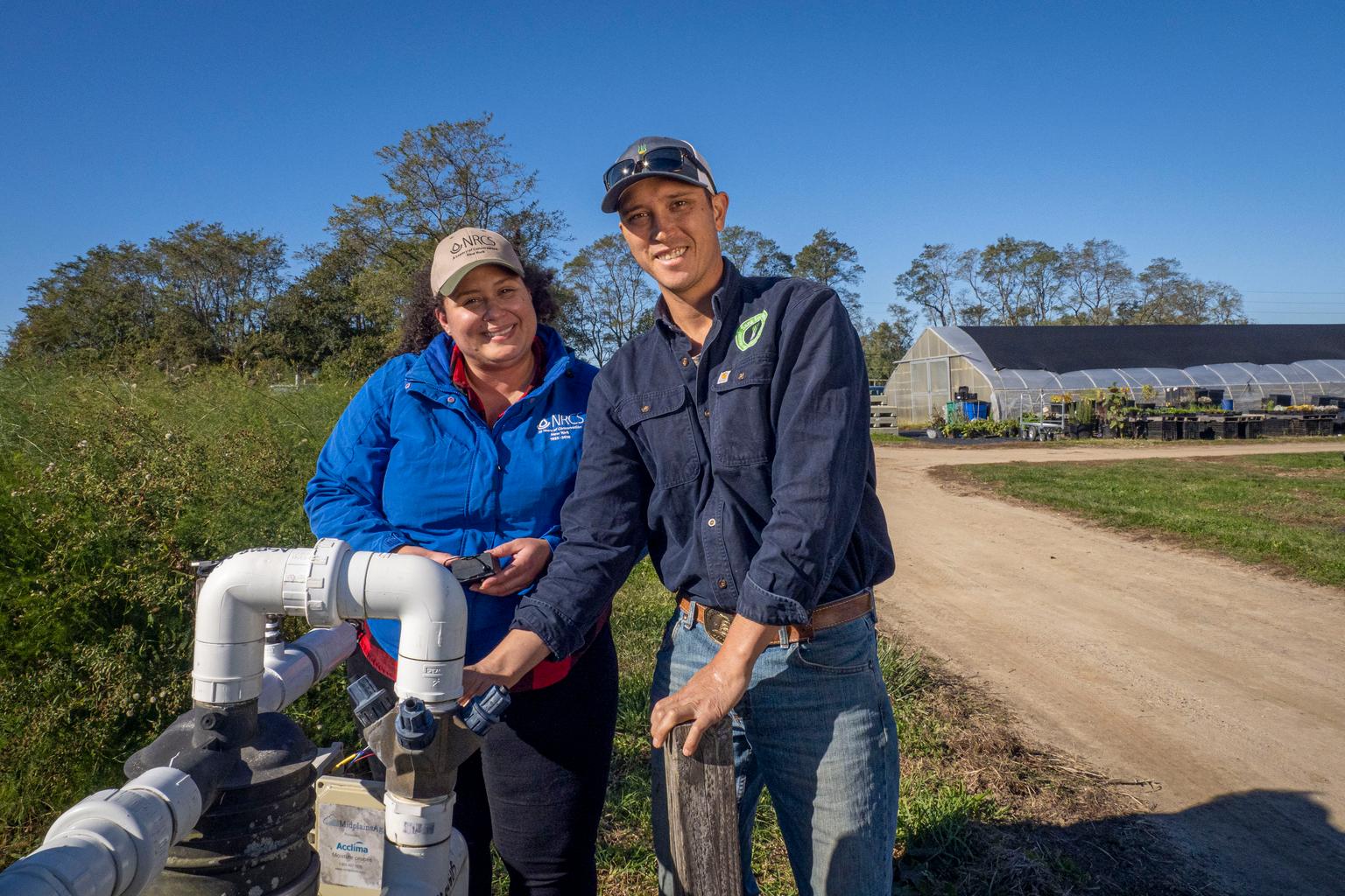 Sang Lee Farms co-owner William Lee and an NRCS district conservationist stand beside irrigation equipment on the family farm in Peconic, New York.