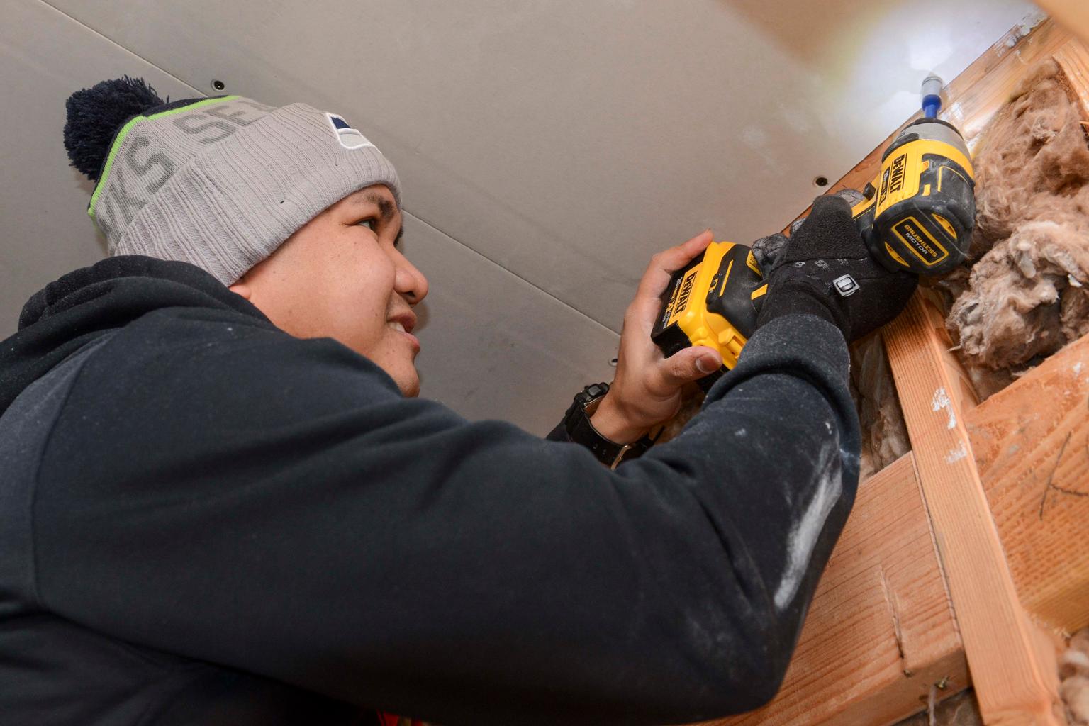 A Habitat for Humanity volunteer uses a drill beside exposed wooden framing and insulation in Port Orchard, Washington.