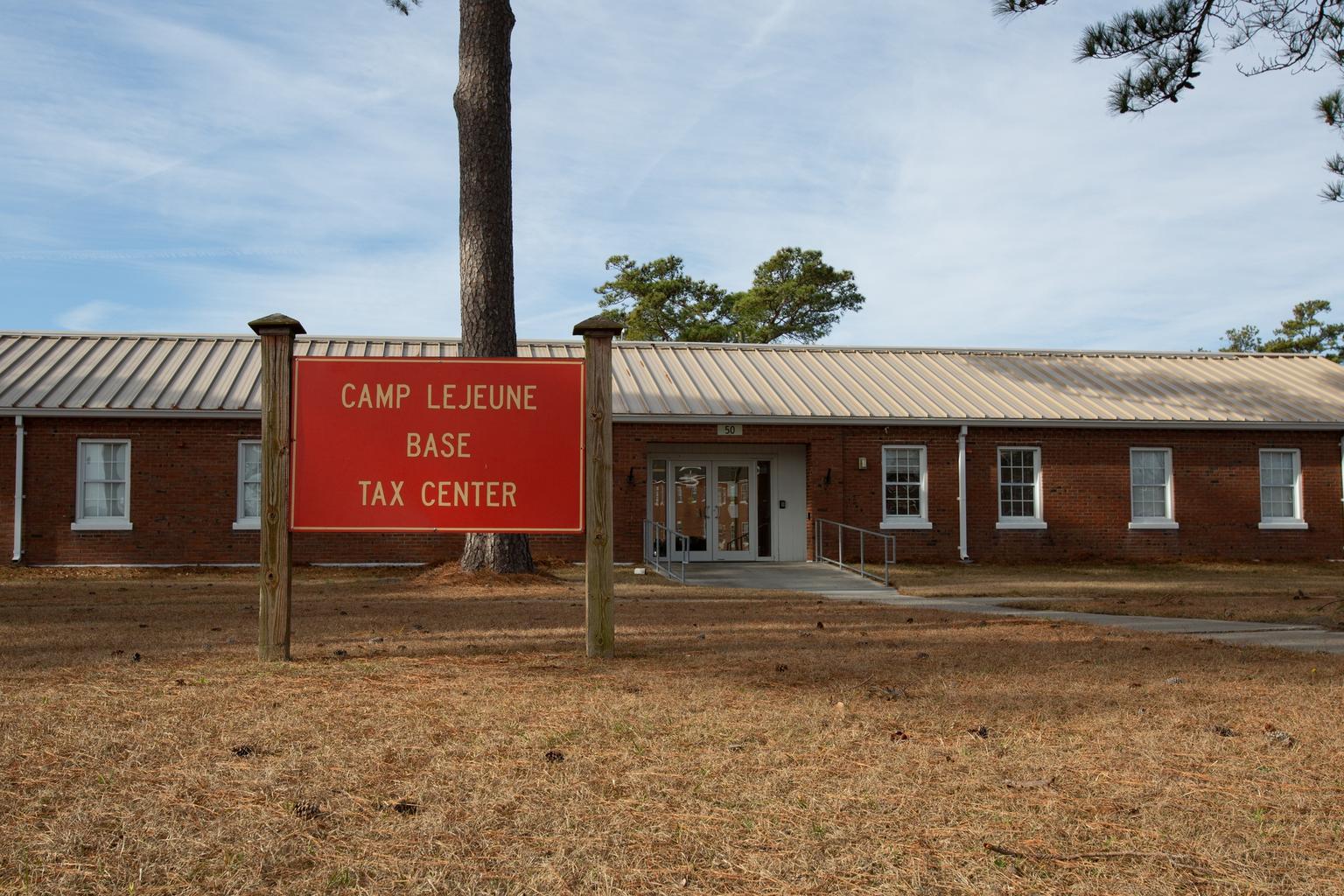 A red Camp Lejeune Base Tax Center sign stands before a brick office building in North Carolina.