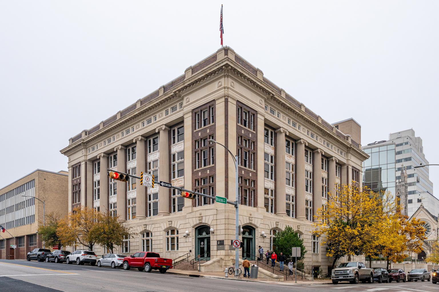 The James E. Rudder State Office Building in Austin stands at a downtown corner beneath U.S. and Texas flags.